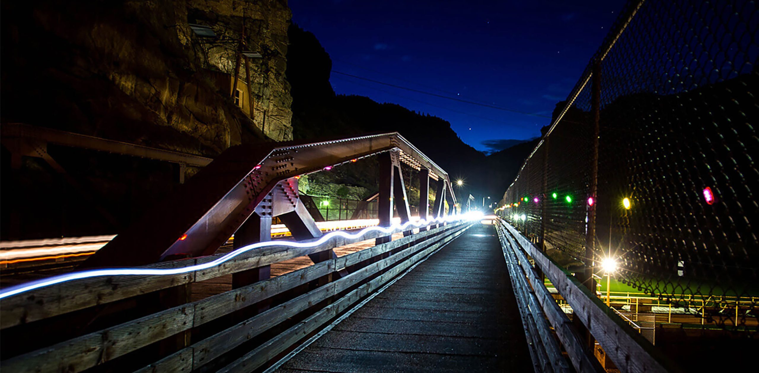 A wooden bridge illuminated by lights against a dark night sky.